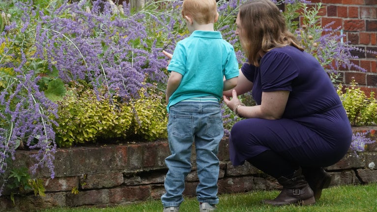 A woman and child look at the border in the garden of Mompesson House. She is wearing a dark blue dress and he has light hair and is wearing a light blue top. He is around five.